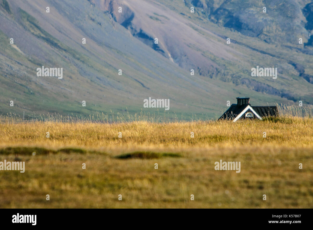 Mountainous landscape with a rural house visible above the field in foreground. Stock Photo
