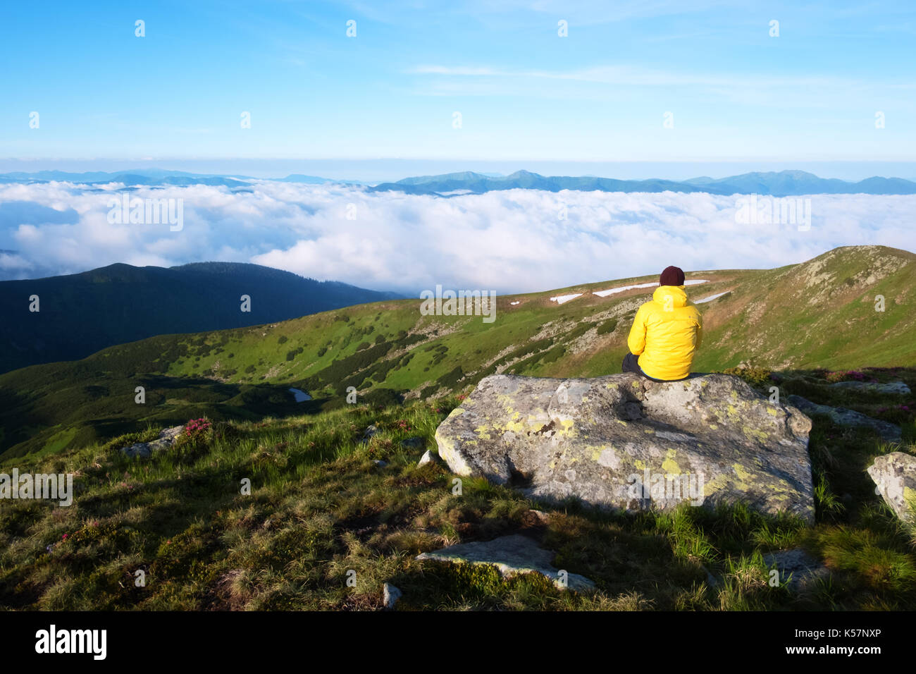 Alone tourist in yellow jacket sitting on rock on high mountains. Stock Photo