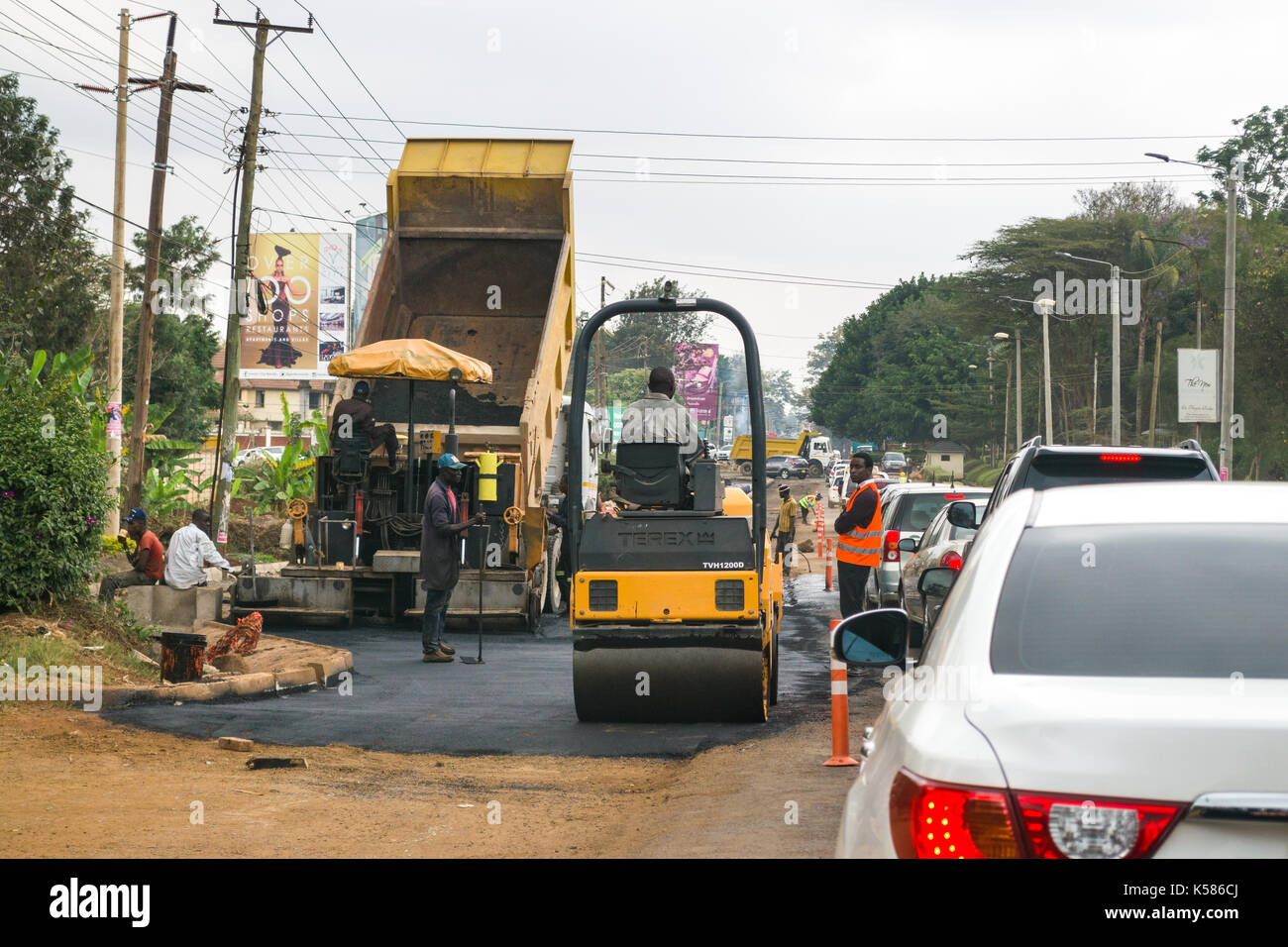 Road construction vehicles pouring tarmac whilst traffic drives past, Nairobi, Kenya Stock Photo