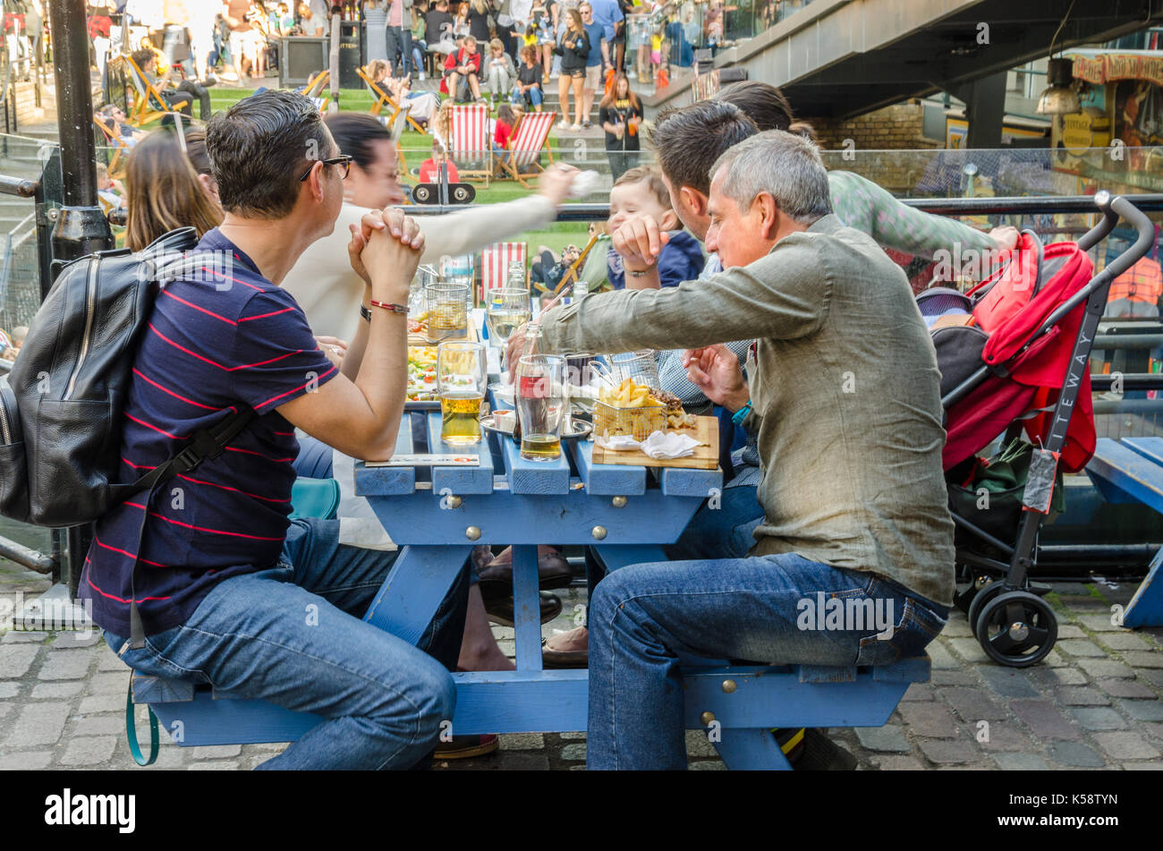 A family sits outside at a trestle table in Camden Market and enjoy food that they have purchased. Stock Photo