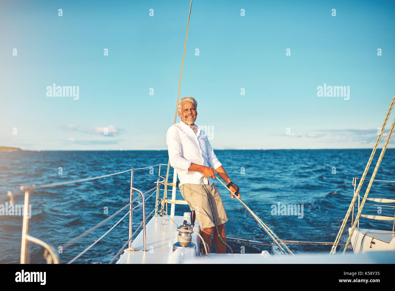 Smiling mature man standing on his boat deck while out for a sail along ...