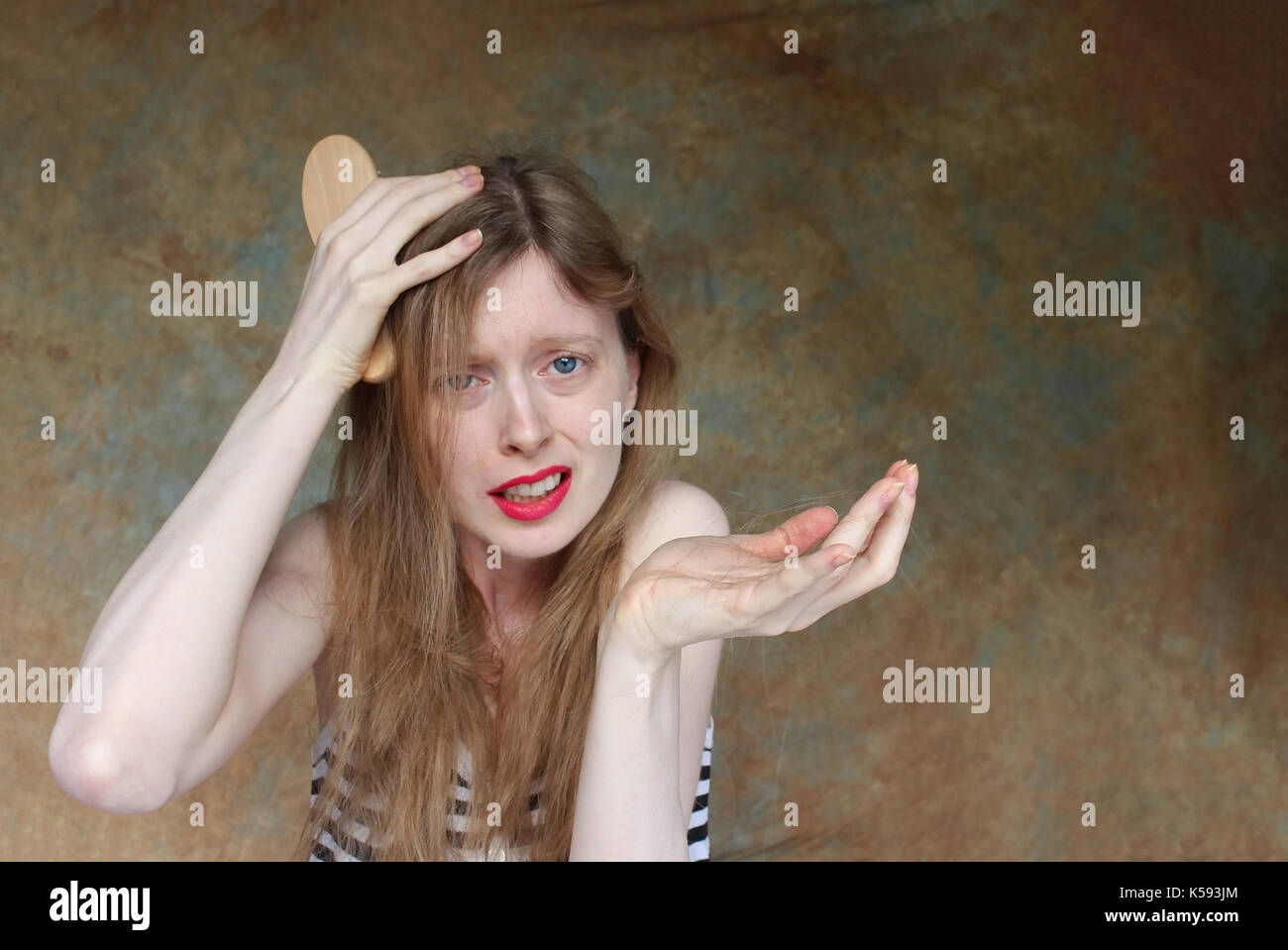 Young woman upset over loosing hair holding fallen out her hand Stock Photo