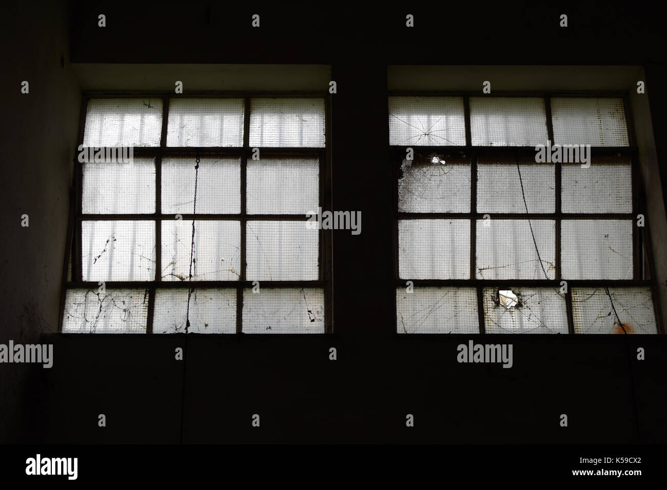 Broken industrial windows in dark abandoned factory interior. Stock Photo