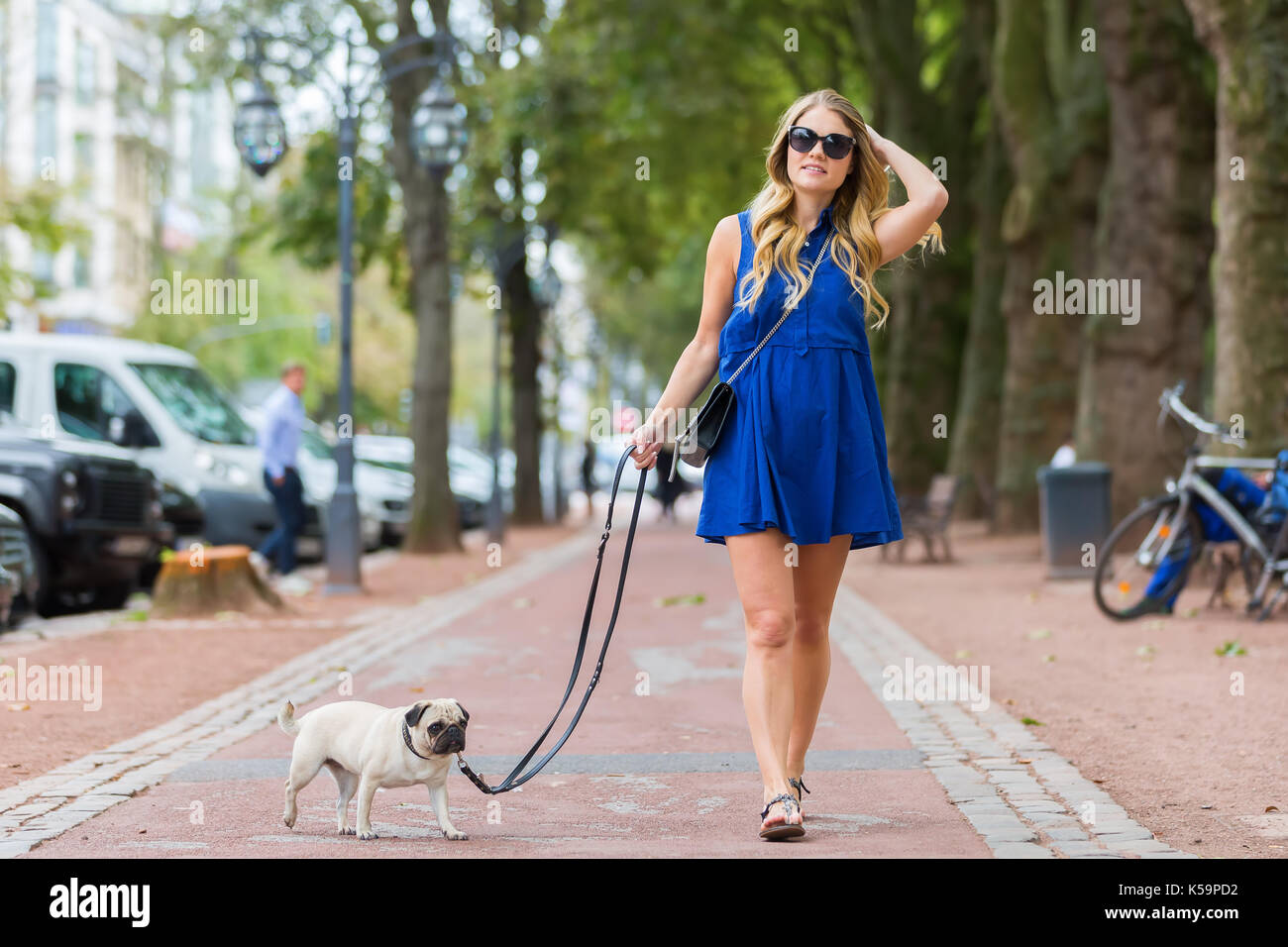 attractive young woman walks with a pug at the leash on a footpath in the city Stock Photo