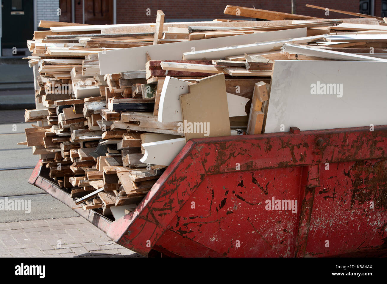 Rust red skip loaded with a pile of old, dirty wood because of home improvement or renovation Stock Photo
