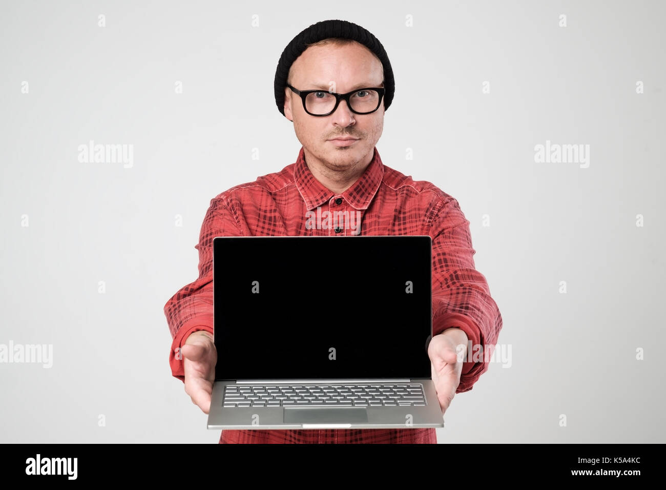 A young programmer in a black hat is holding a laptop in his han Stock Photo
