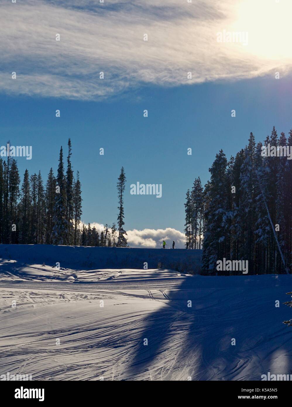 Two skiers in distance crossing ridge at ski hill in winter Stock Photo
