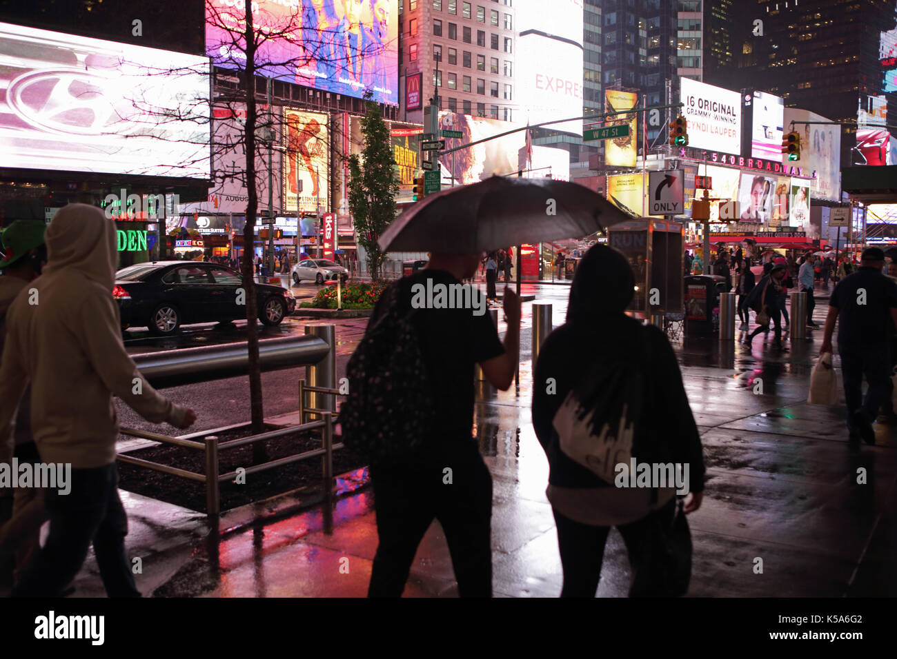 Rainy night in Times Square, tourists with umbrellas walk 7th Avenue