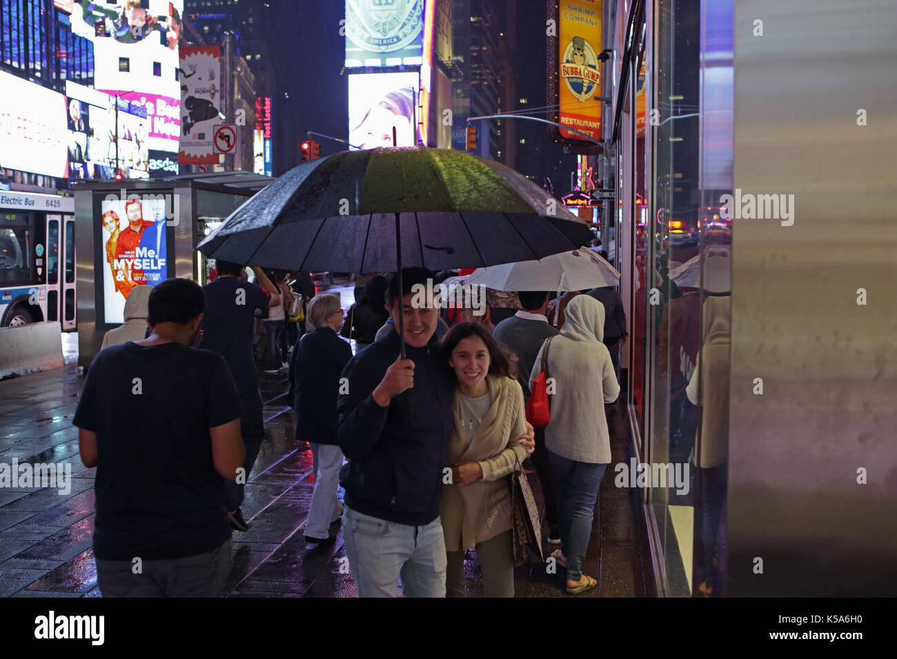 Rainy night in Times Square, tourists with umbrellas walk 7th Avenue and Broadway brightly lit by electric billboard advertising screens Stock Photo
