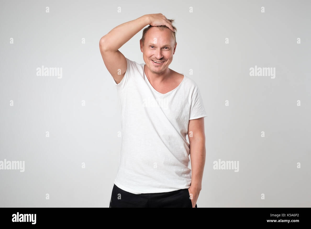 Smiling young man in white t-shirt standing against white background Concept of self confident man. Stock Photo
