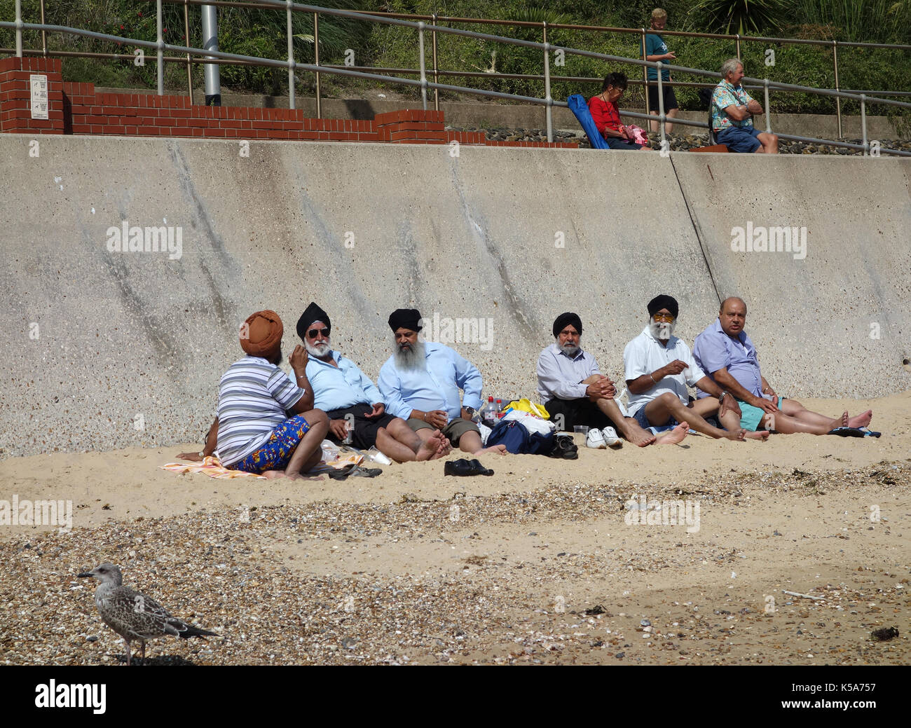 Group of elderly Sikh men sitting on beach at Clacton-on-Sea Stock Photo