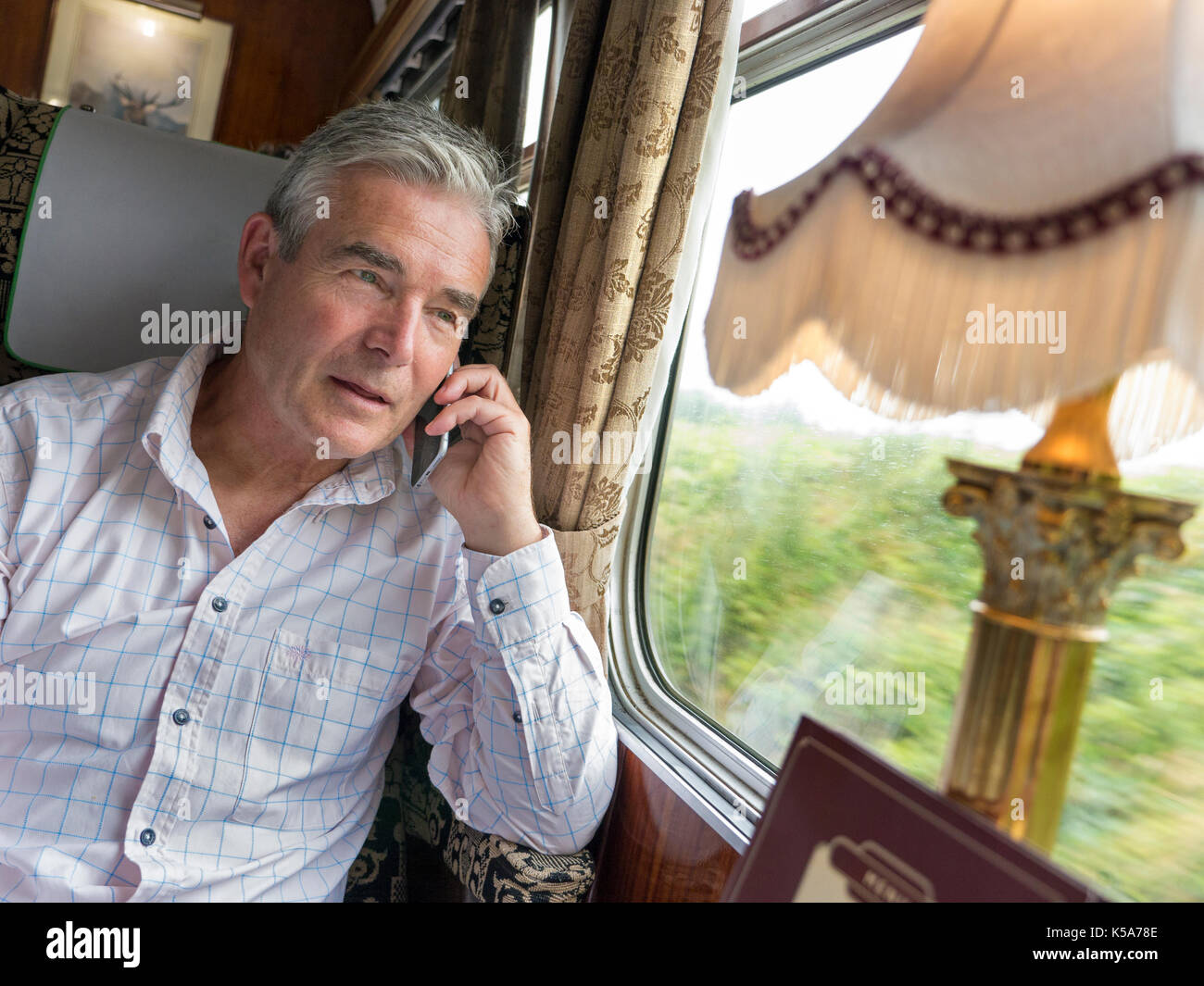 Relaxed mature man in first class restaurant rail car talking on his iPhone 6, enjoying a train trip in a luxury vintage Pullman railway carriage Stock Photo