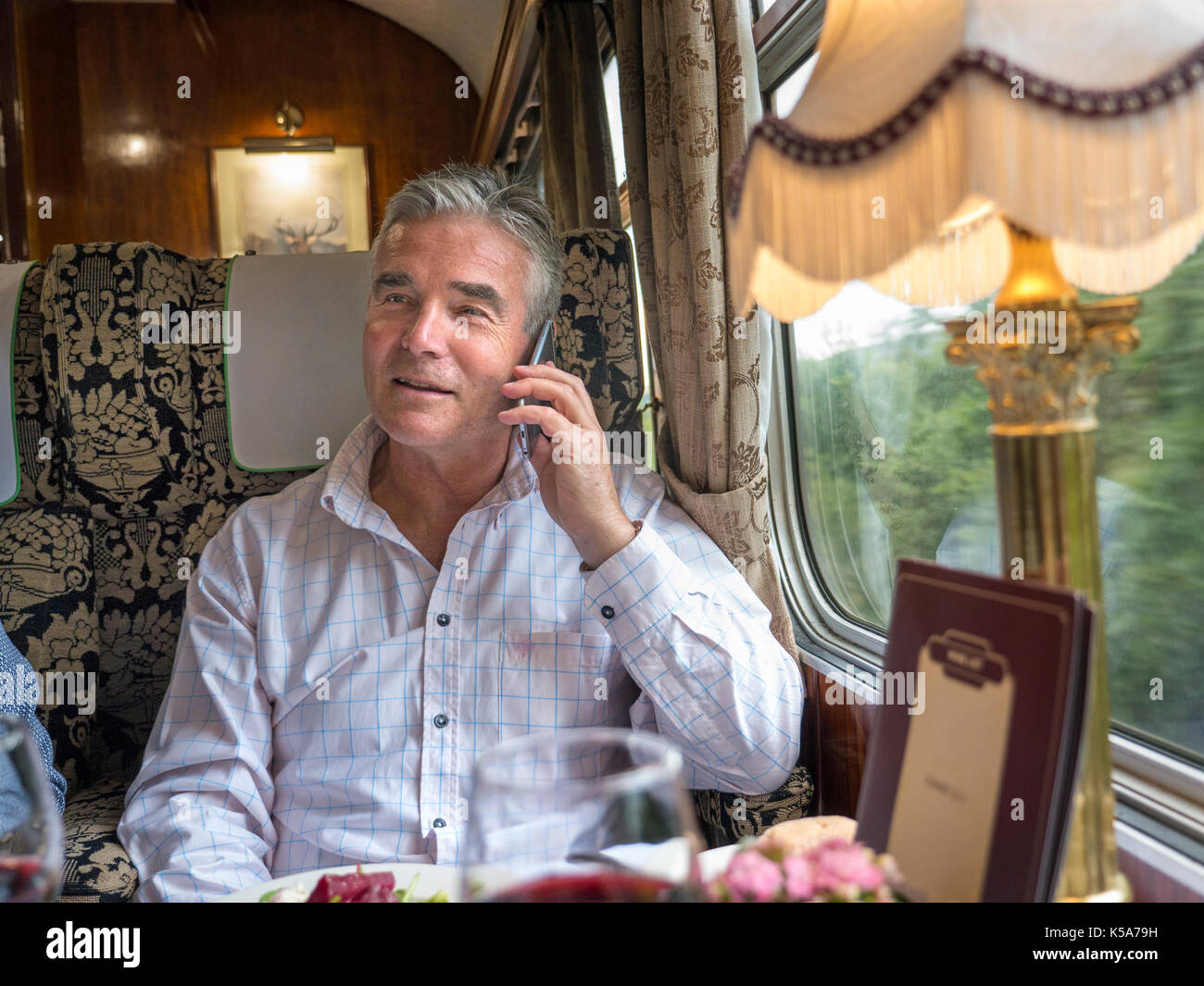 LUXURY First class train carriage & businessman in restaurant rail car talking on smartphone enjoying train trip in a luxury Pullman railway carriage Stock Photo