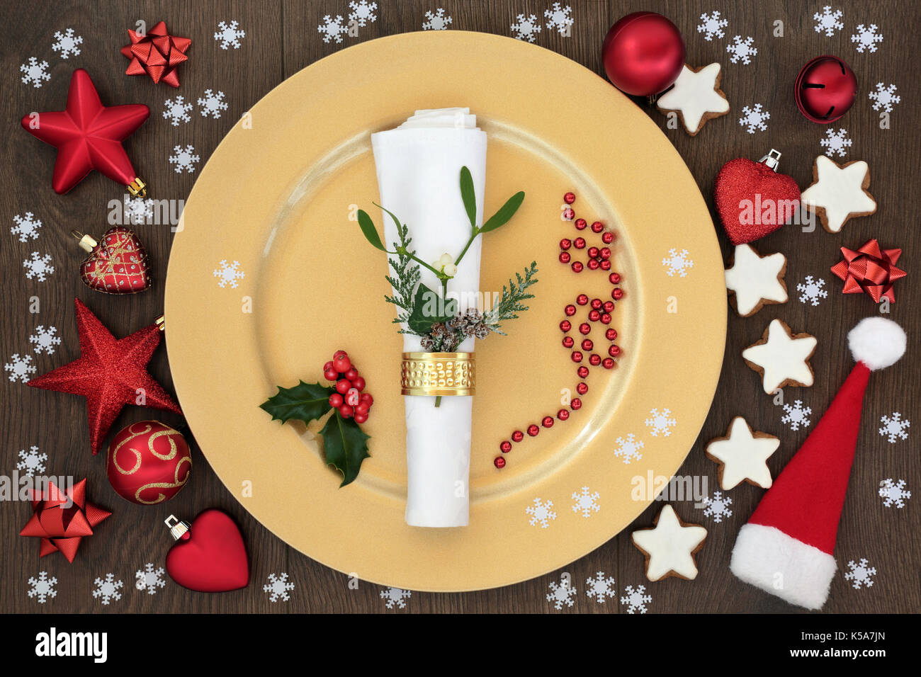 Christmas table place setting with gold dinner plate, napkin with cedar, mistletoe and holly, santa hat, gingerbread biscuits and bauble decorations o Stock Photo