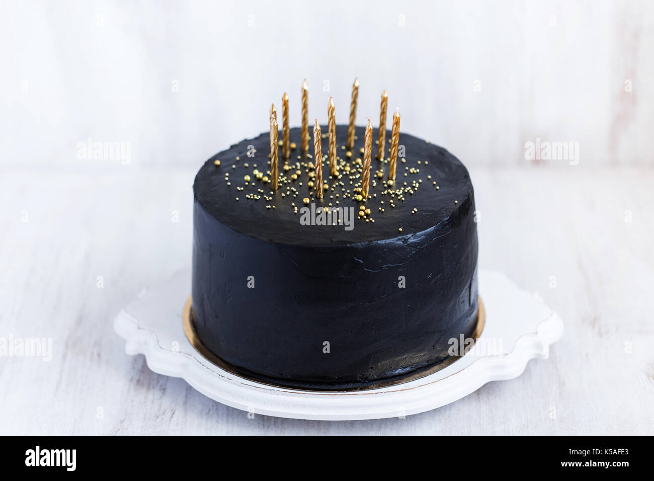 Black birthday cake with golden candles on white background Stock Photo ...