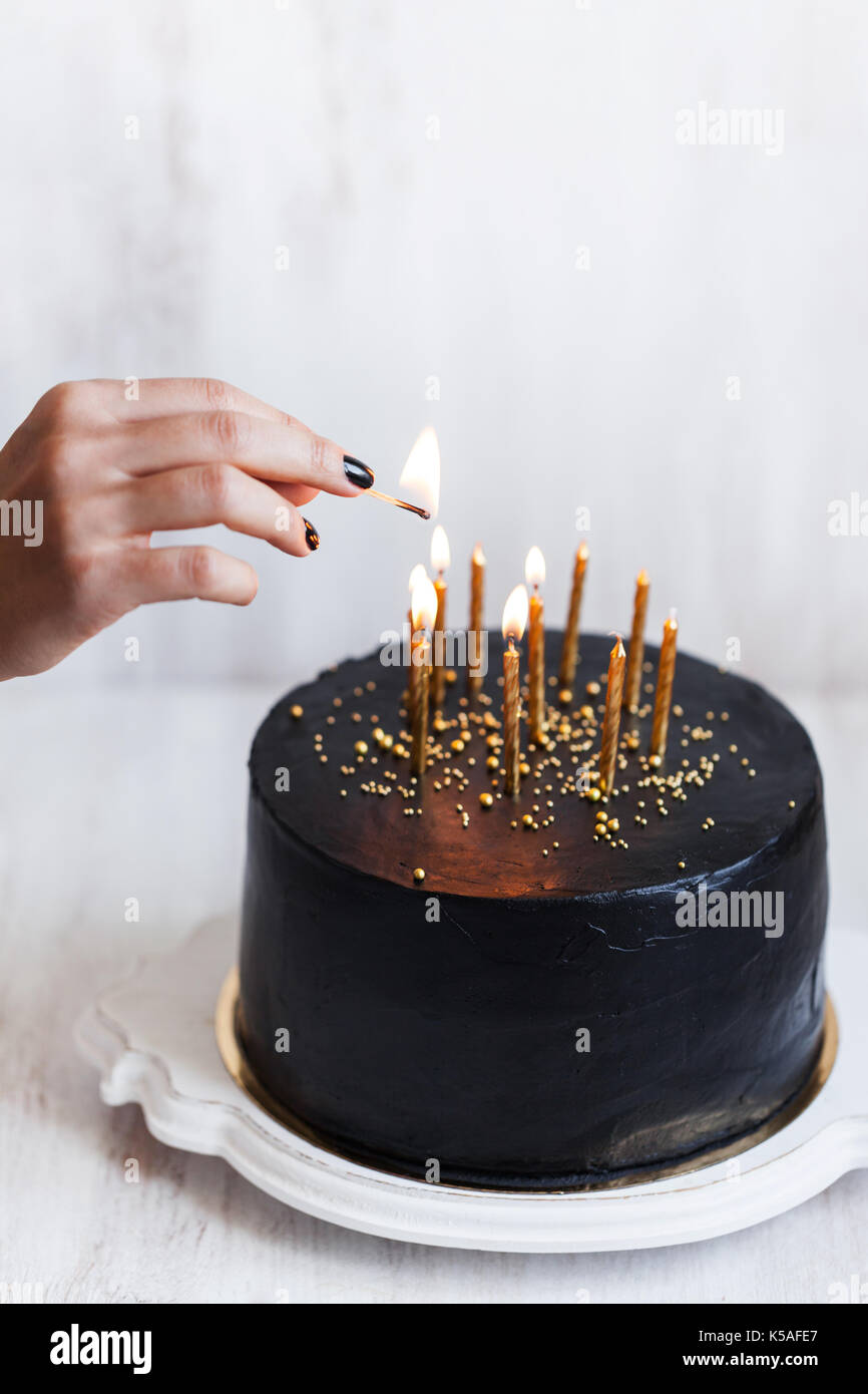 Black birthday cake with woman hand burning candles, white background