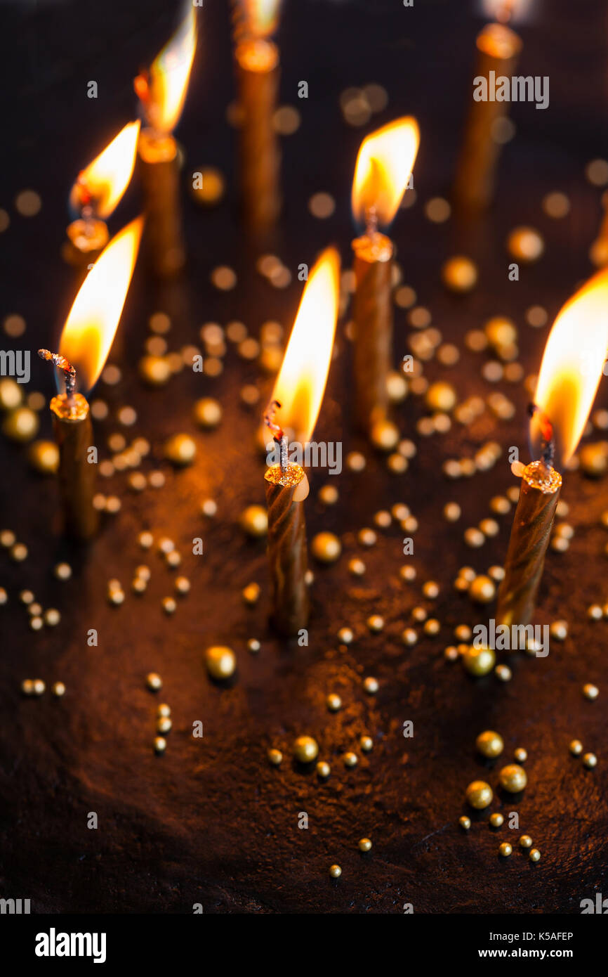 Black round birthday cake with burning golden candles on white ...