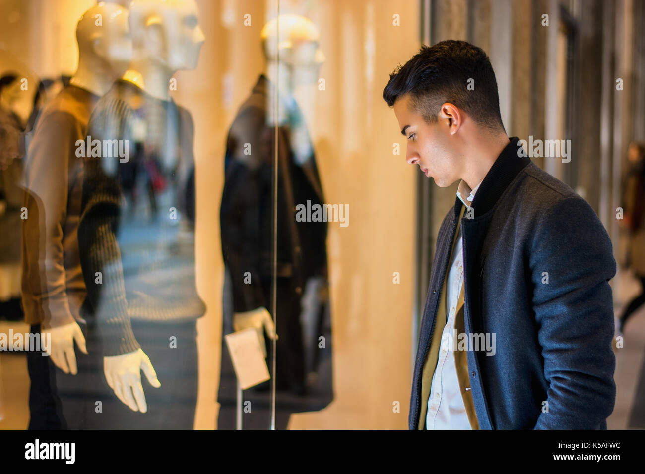 Handsome Young Man in Black Elegant Suit Looking at Displayed Fashion Items in Glass Window Boutique at the High Street Side. Stock Photo