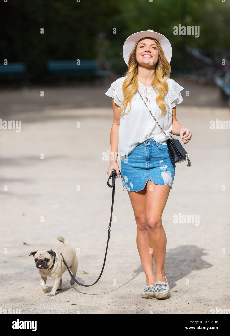 attractive young woman walks with a pug at the leash in the park Stock Photo