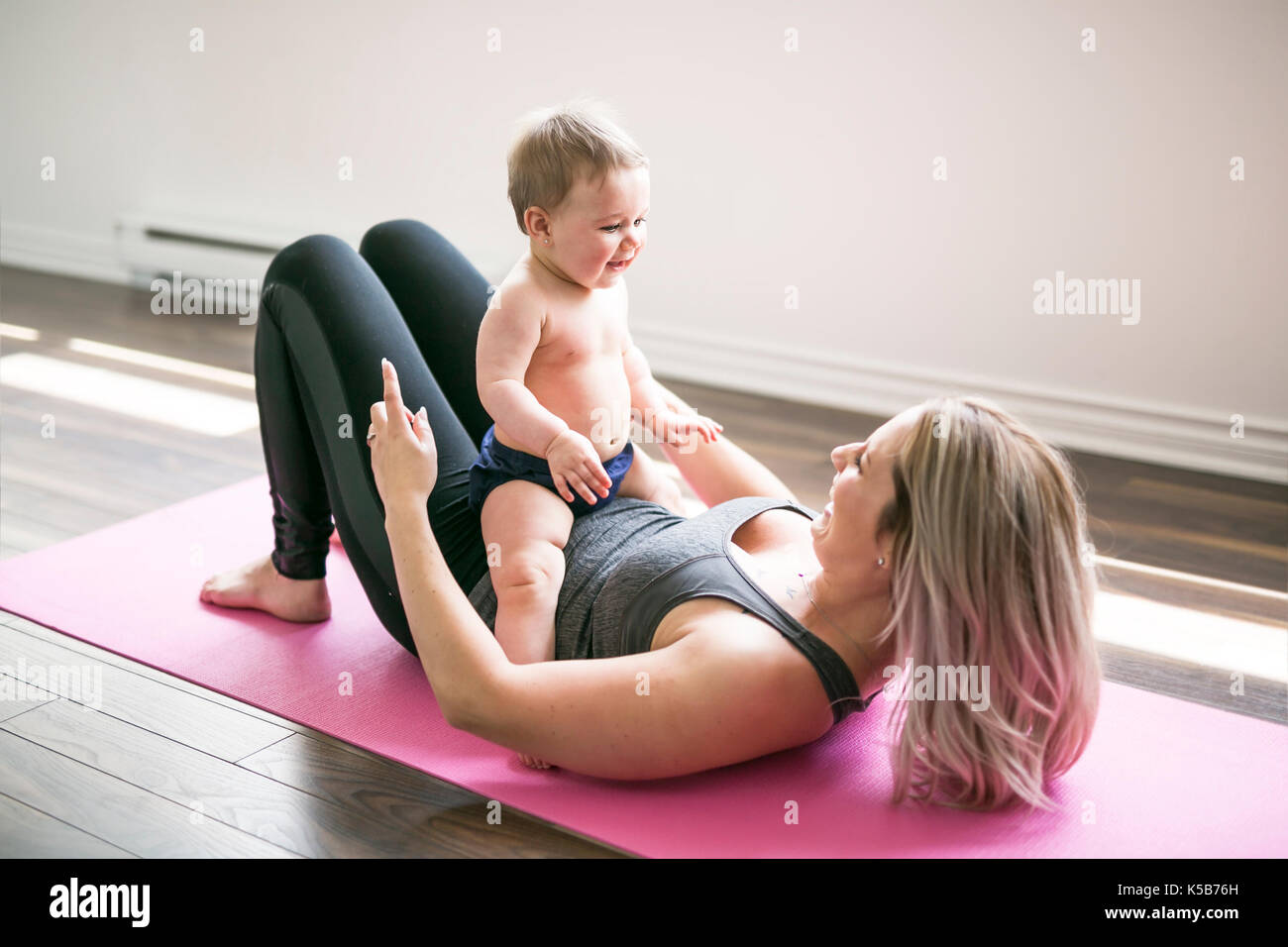 Adorable little child doing splits with mother's support while following  on-screen instructor at home. Happy caucasian ladies in black wear enjoying  baby yoga without leaving comfort of room Stock Photo - Alamy