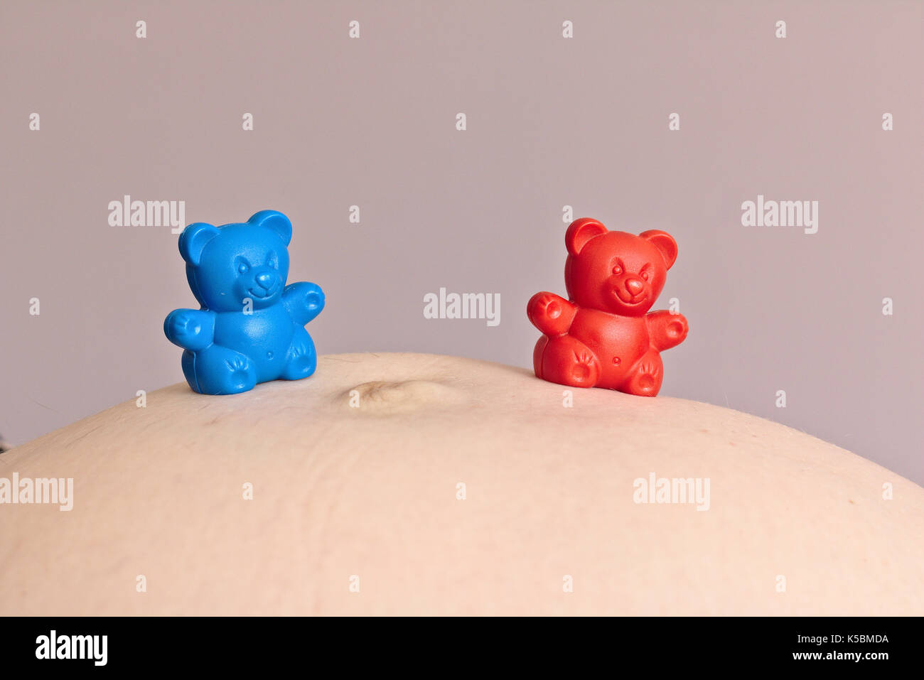 Red and blue plastic toy bear on pregnant woman's belly Stock Photo