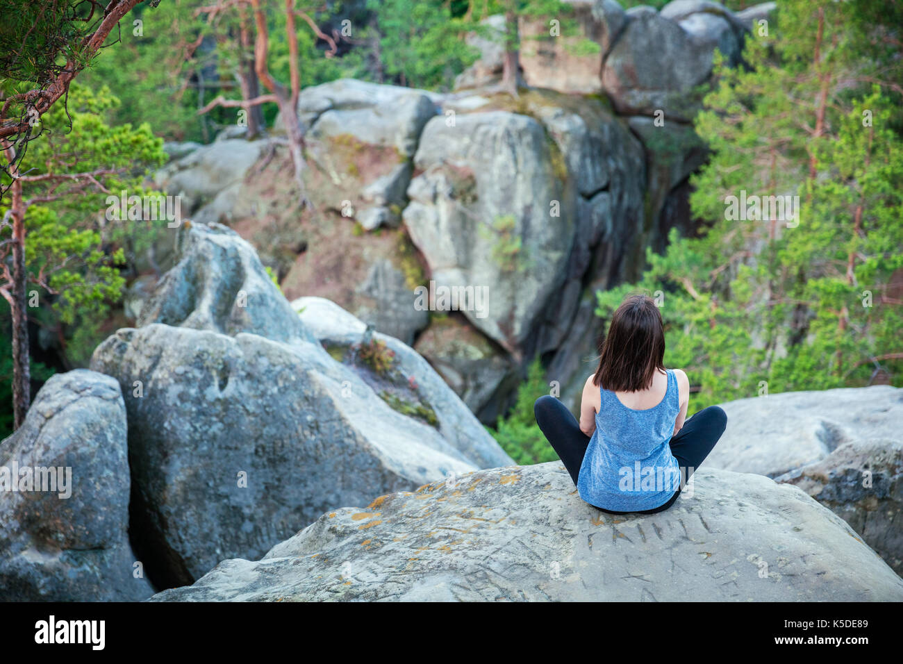 Young girl sitting on top of cliff and watching rocky landscape beneath Stock Photo