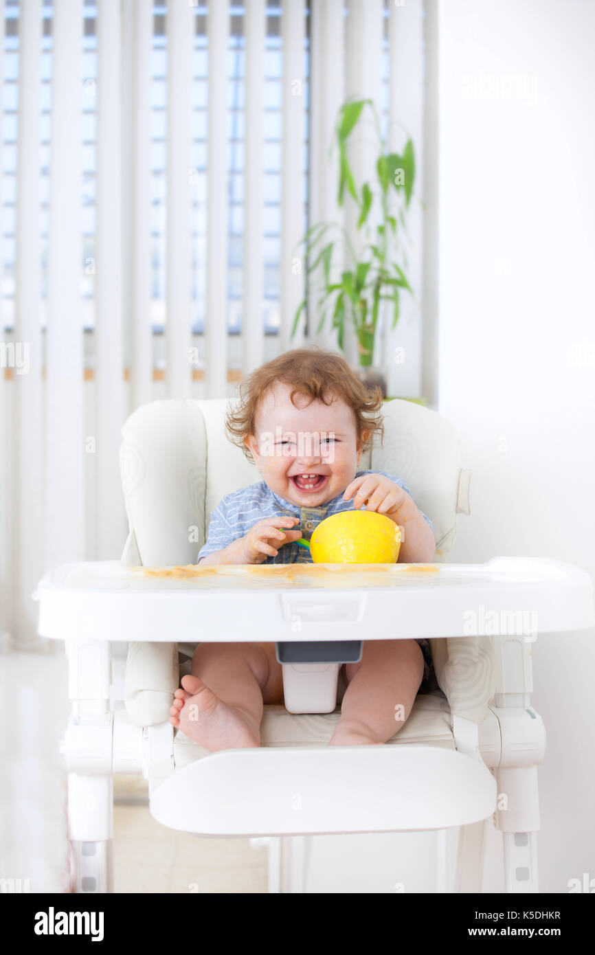 Cute baby boy eating by himself on high chair Stock Photo