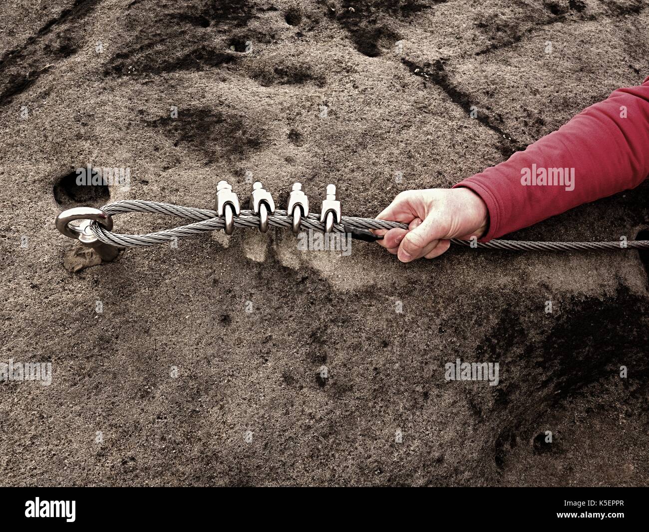 Rock climber hand hold on steel twisted rope at steel bolt eye anchored