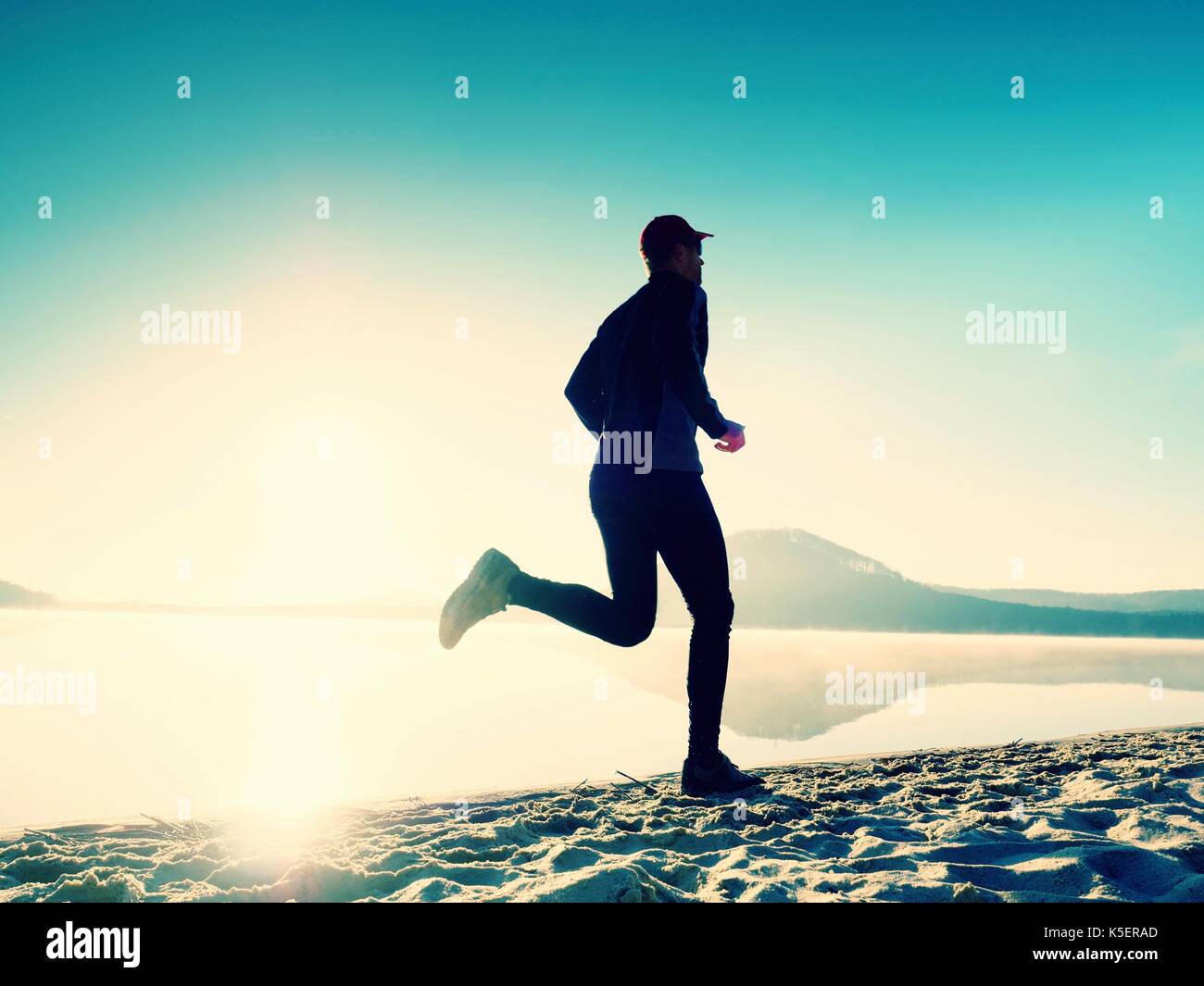 Silhouette of sport active man running on the lake beach at sunrise ...