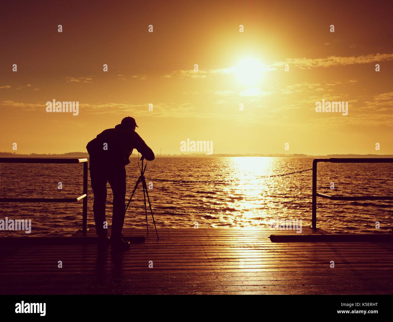 Photographer takes photos with mirror camera and tripod at end of pier ...