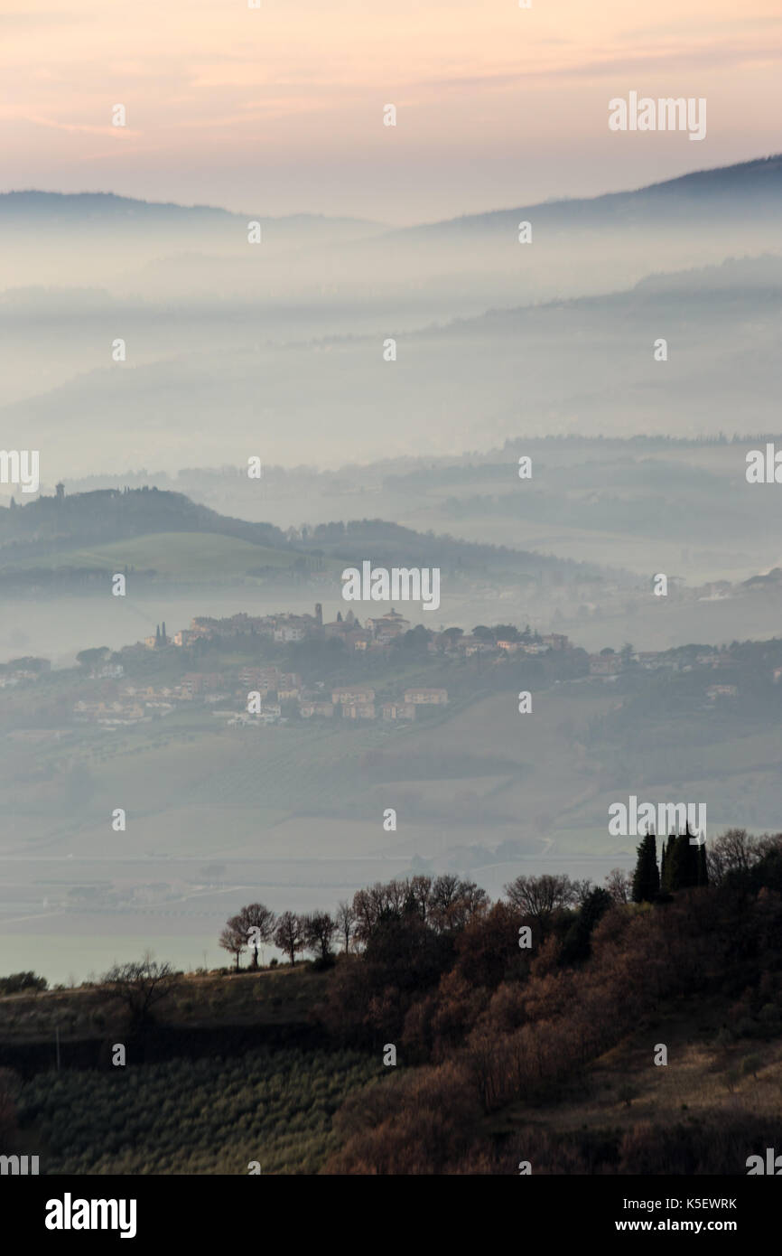 A view of some trees in the foreground with layers of hills and towns through the mist in the background Stock Photo