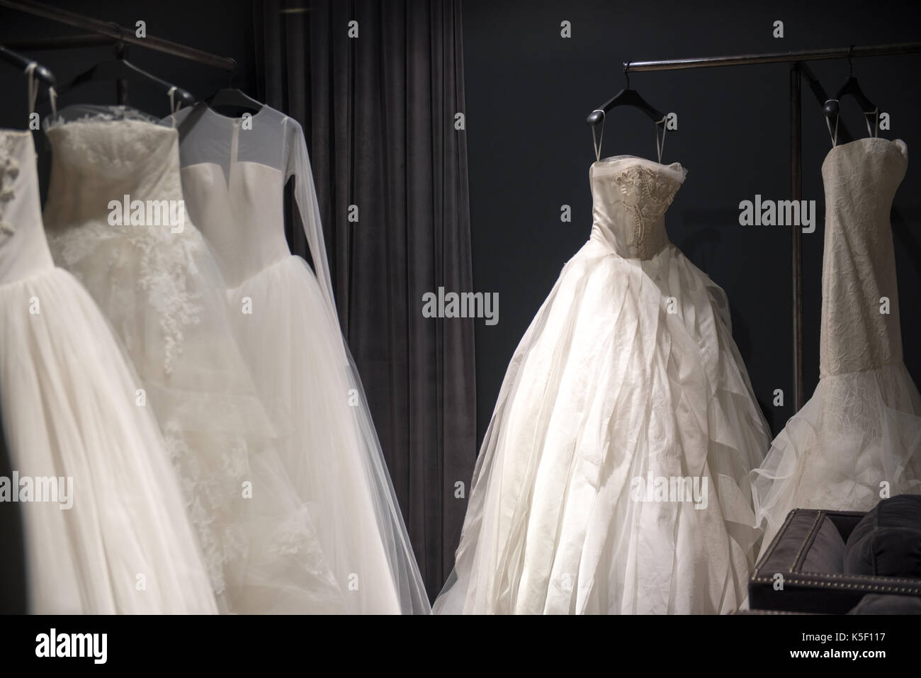 Selection of white wedding dresses or ball gowns on display hanging on rails with selective focus to one illuminated by a highlight Stock Photo