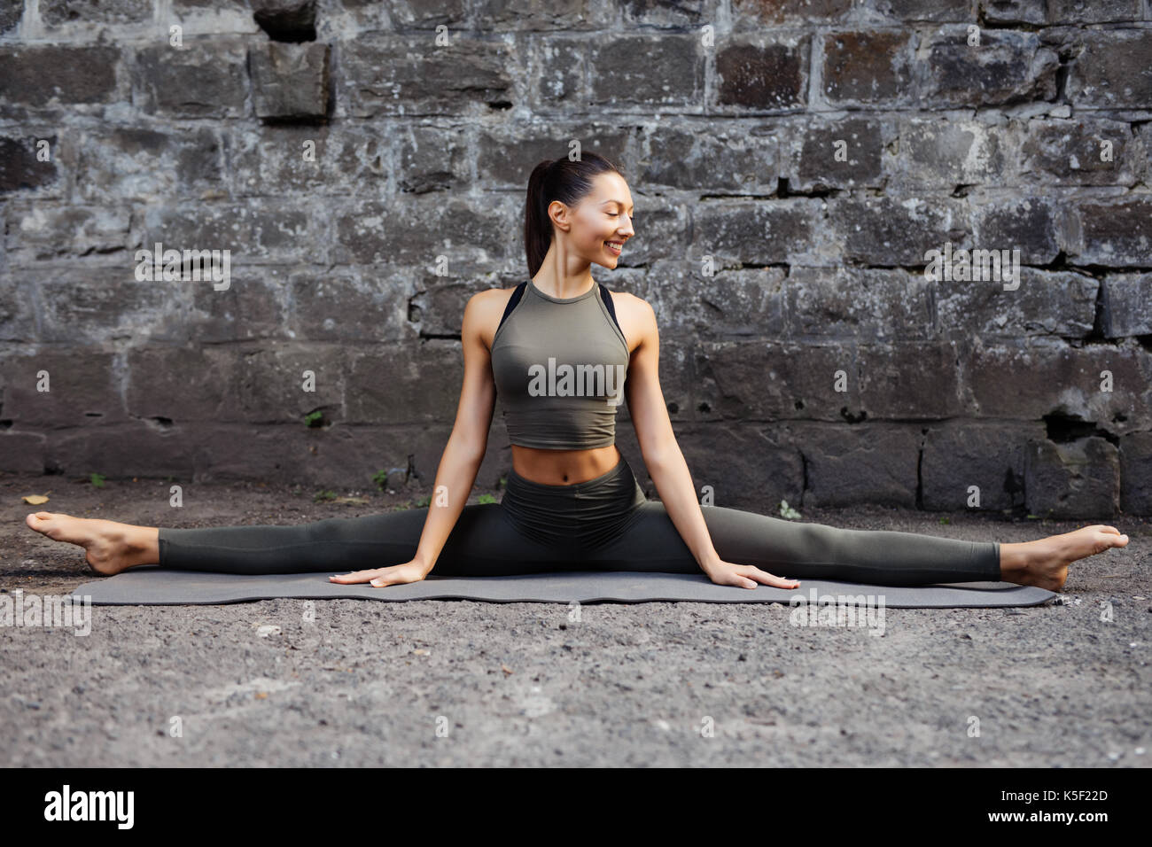 Sporty beautiful young woman practicing yoga working out, wearing sportswear, outdoor full length, brick wall Stock Photo