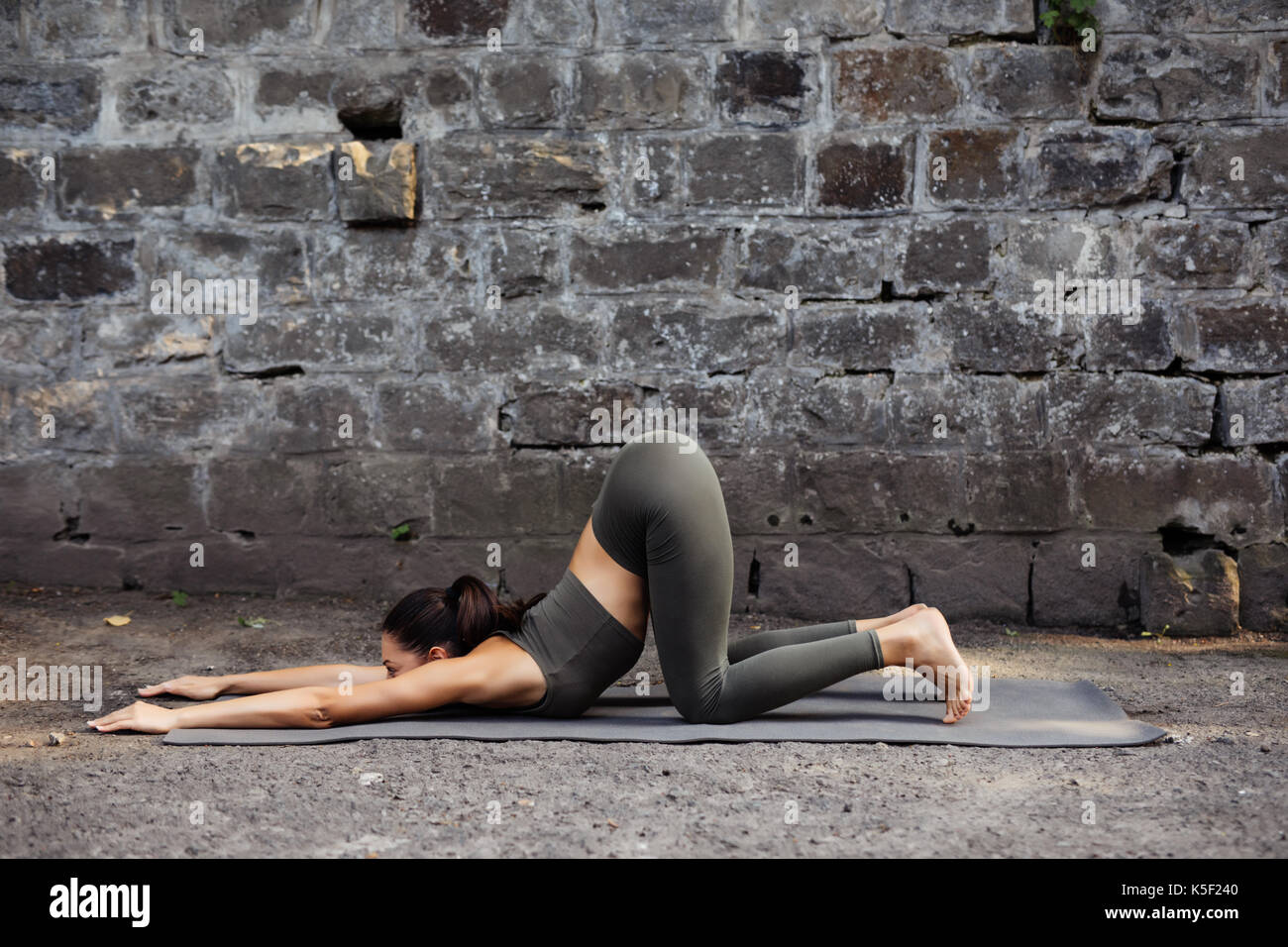 Sporty beautiful young woman practicing yoga working out, wearing sportswear, outdoor full length, brick wall Stock Photo