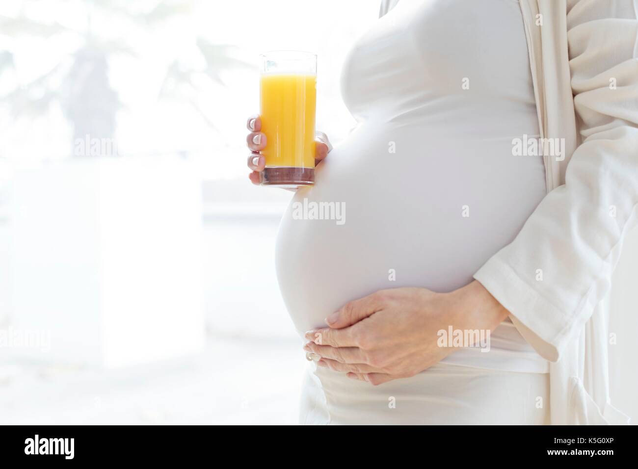Pregnant woman touching tummy holding glass of fruit juice. Stock Photo