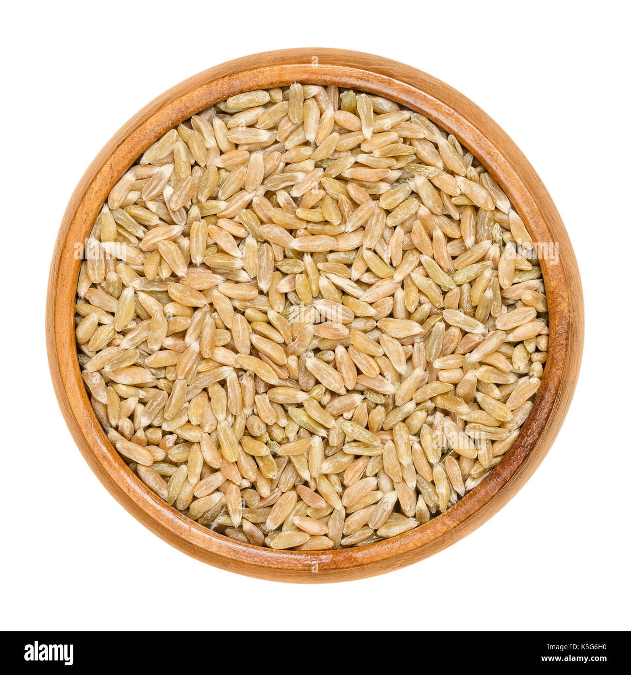 Whole grain green spelt in wooden bowl. Husked, dried half ripe spelt. Green kernel. Seeds of Triticum spelta, also dinkel wheat or hulled wheat. Stock Photo