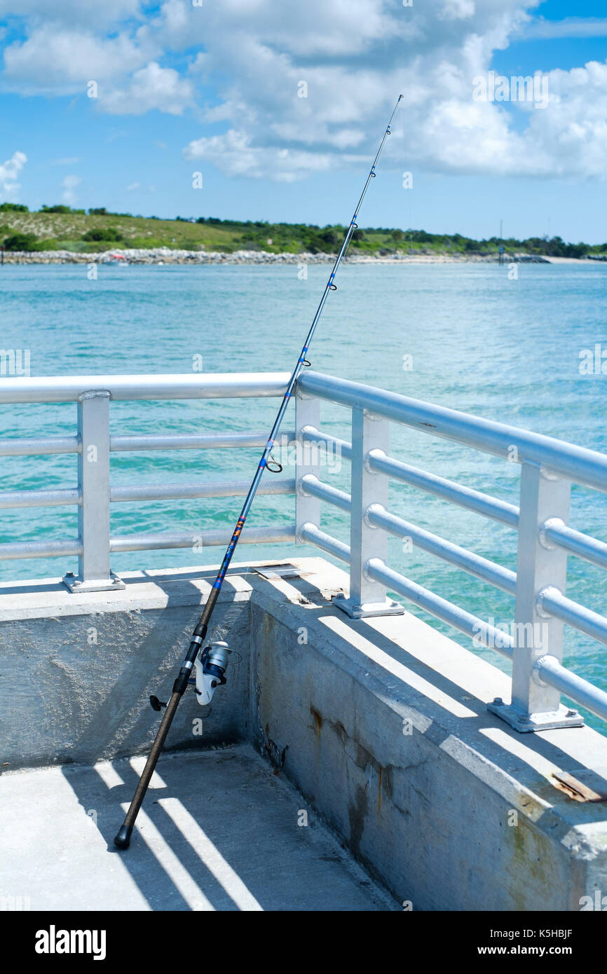 single fishing rod resting against pier raling against backdrop of