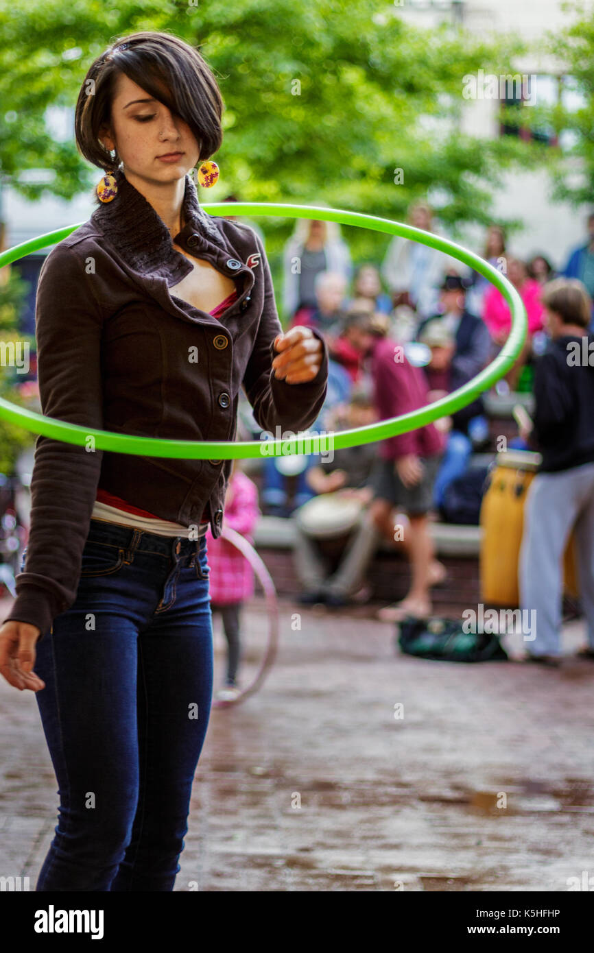 An adolescent girl hula hoops, alone in a crowd, at the drum circle at