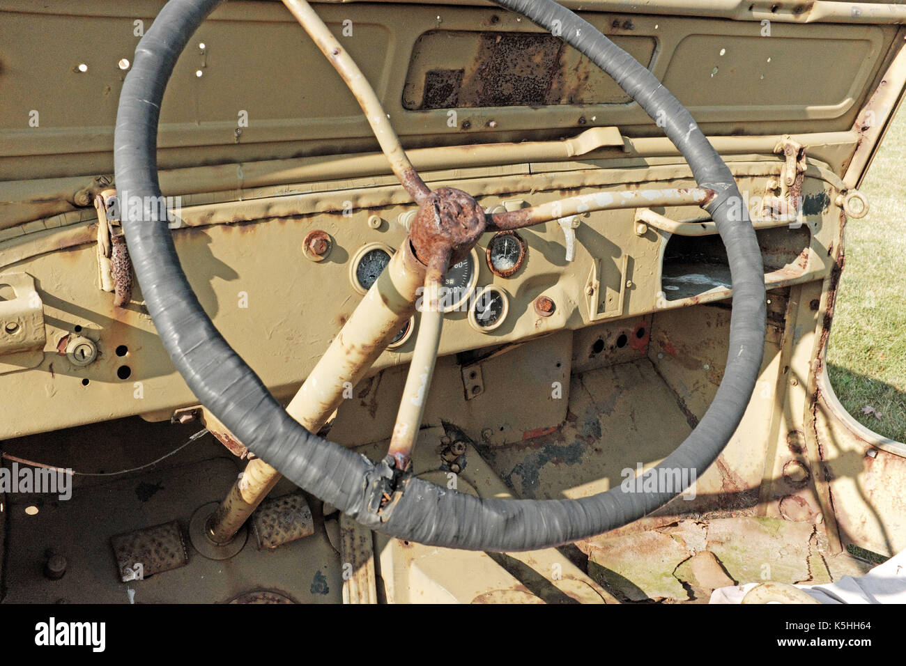Vintage military jeep open front cabin, dashboard, and steering wheel showing their rust from the elements. Stock Photo