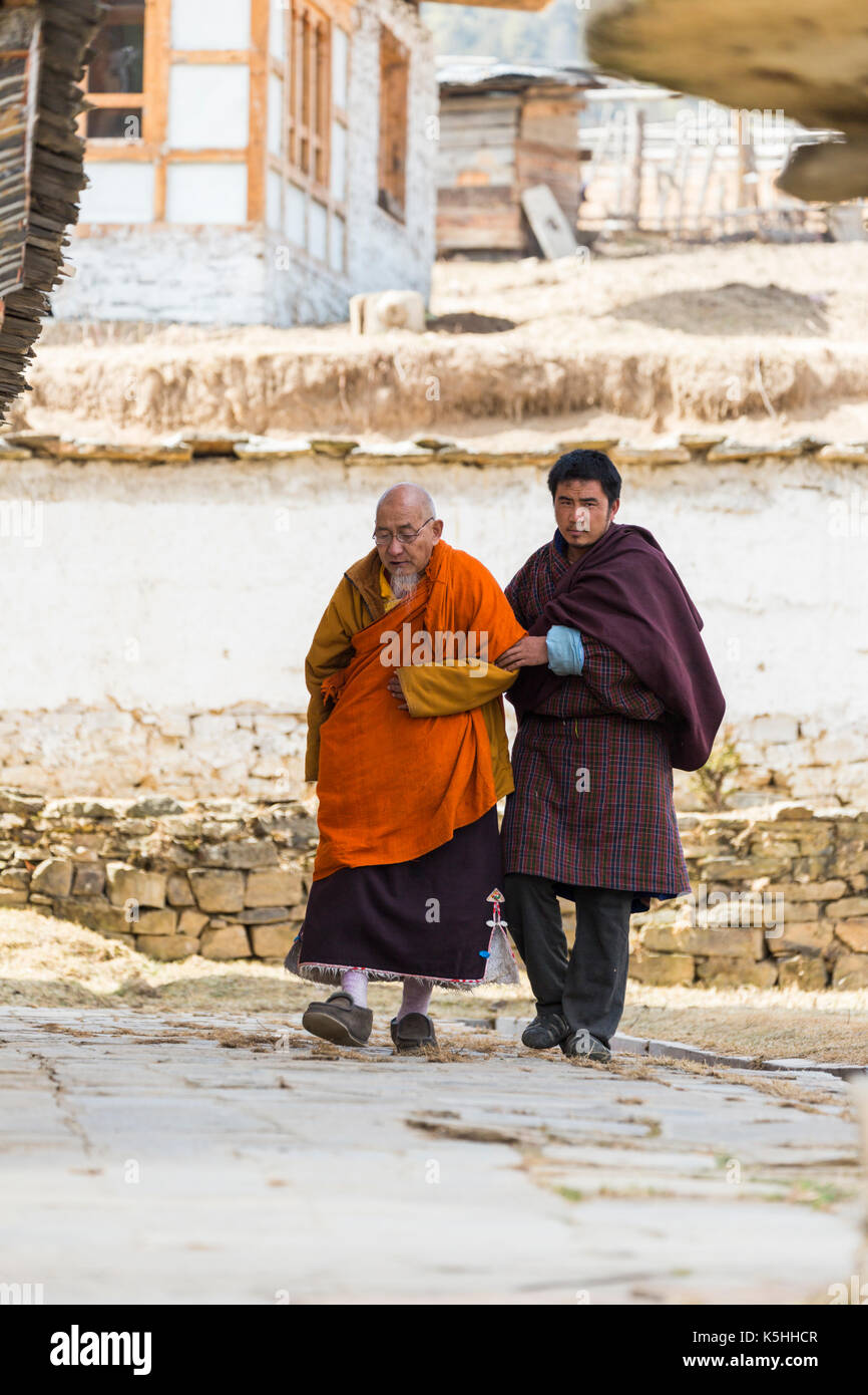 Villager assists senior monk outside the Buddhist temple in Ura, (Ura Mang Gi Lakhang) Central Bhutan. Stock Photo