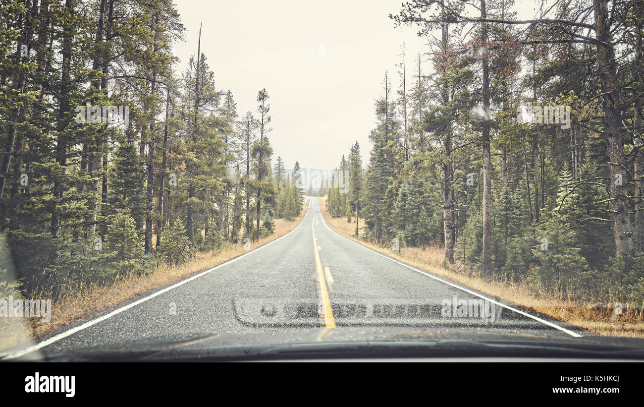 Mountain rainy road seen through the windshield, color toning applied, travel concept. Stock Photo