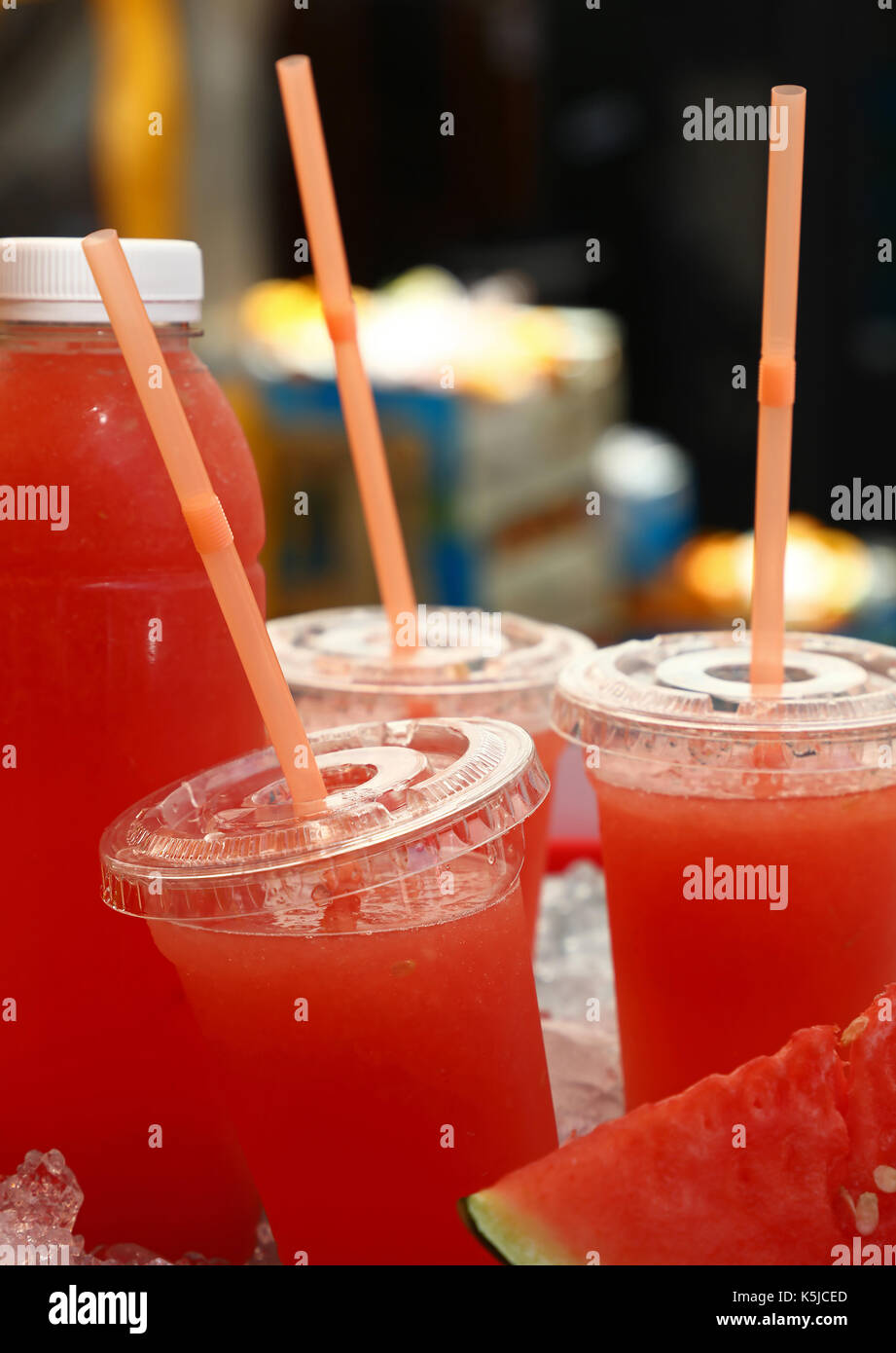 Fresh squeezed red ripe watermelon juice in plastic cups with straws and bottle on ice in retail market stall display, close up, low angle view Stock Photo