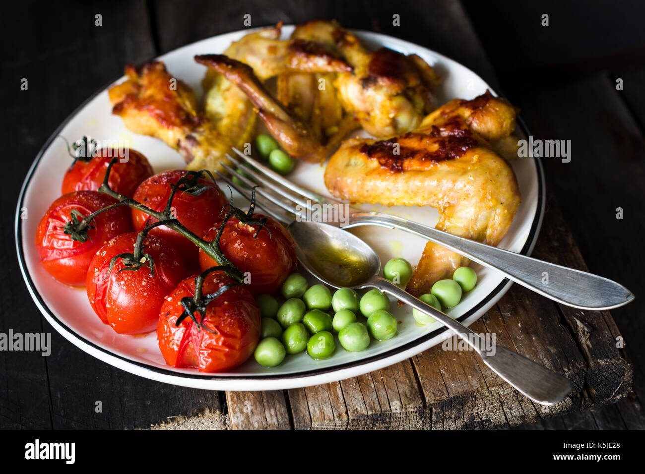 Spicy chicken wings, roasted cherry tomatoes and sauteed green peas on white plate. Baslanced meal. Closeup view, selective focus Stock Photo