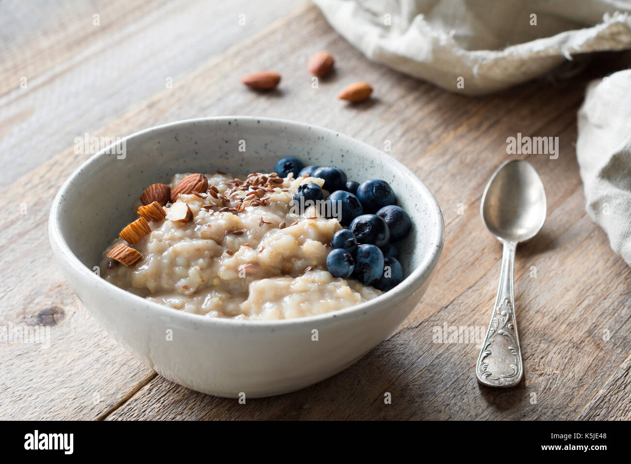 Oatmeal porridge with blueberries, almonds, linseeds in bowl on wooden table. Super food for healthy nutritious breakfast Stock Photo