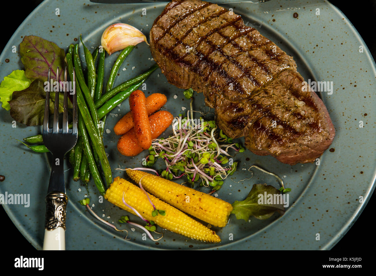 Grilled beef steak with glazed vegetables on the black background Stock Photo