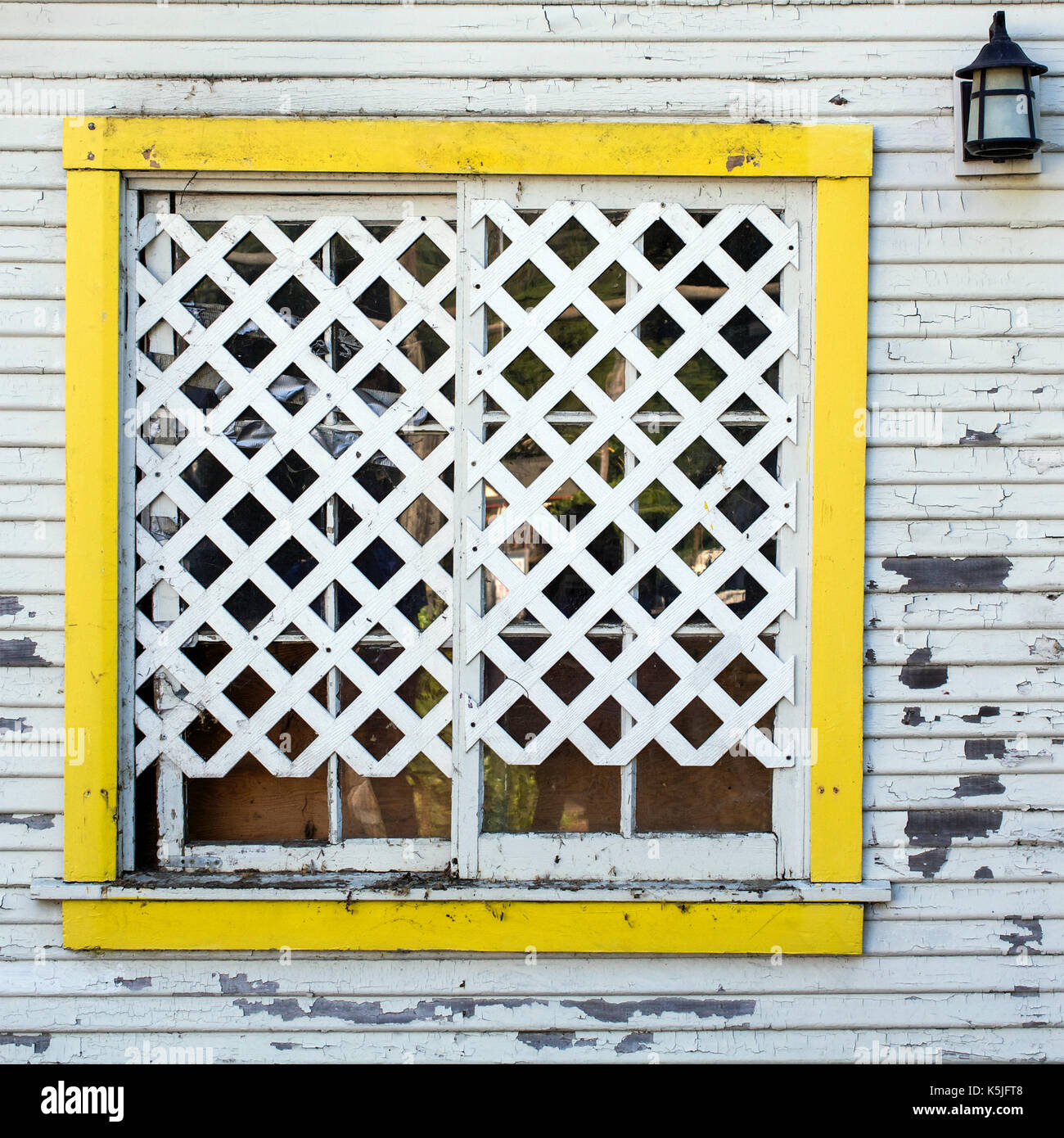Detail on the white wall of an old wooden house featuting yellow frame lattice window and lantern Stock Photo