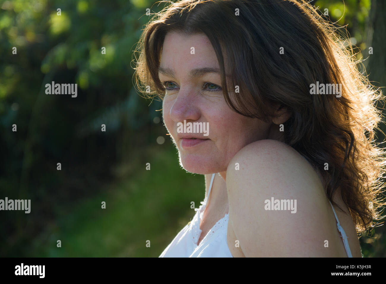 A pretty middle aged woman with brunette hair relaxes in the shade of a tree on a sunny, late-summer afternoon.  Shropshire, UK. Stock Photo