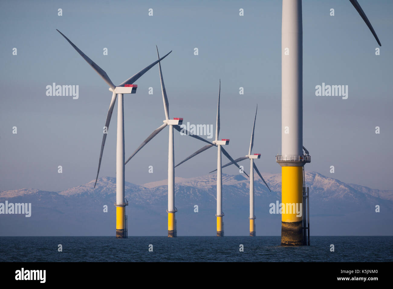 Wind turbines of Walney & West of Duddon Sands Offshore Wind Farm with snow-capped hills of the Lake District in the background Stock Photo