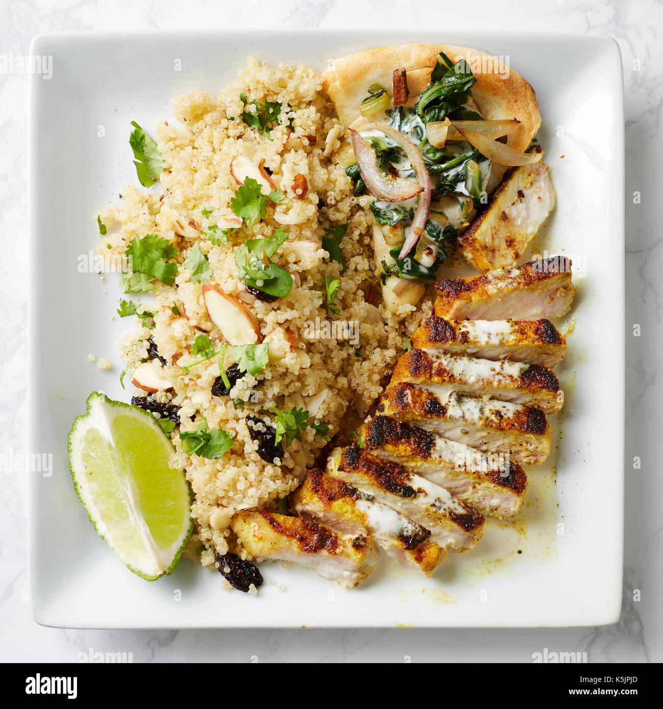 Grilled pork or chicken, quinoa and flatbread meal with fresh lime on a square white plate Stock Photo