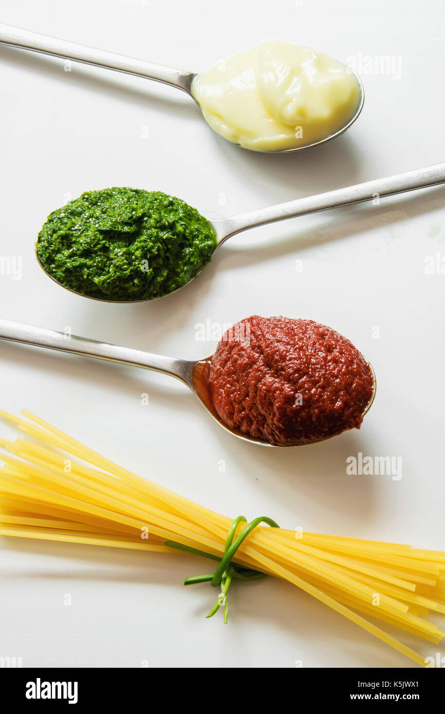 Spaghetti and three spoons with different condiments tomato sauce